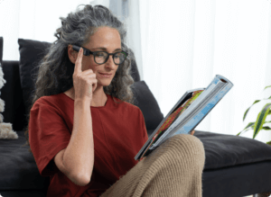 A lady with grey hair and glasses using the OrCam MyEye to read a magazine