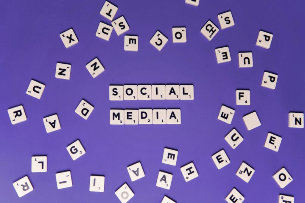 Scrabble tiles spread out in a circle on a purple background. In the middle are tiles that spell out social media.