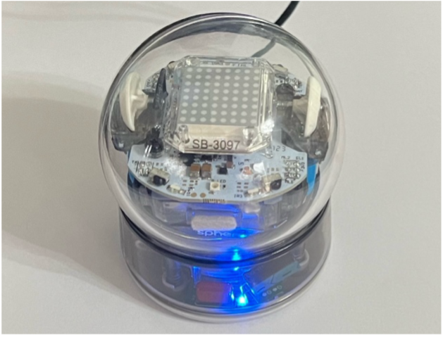 Bolt Robot, switched on with a bright blue LED. The Robot is a clear plastic sphere. inside you can se a motor and an aray of sensors.